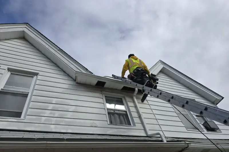 Technician on a ladder at the roof edge of a house